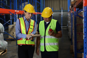 Group of warehouse workers with hardhats and reflective jackets using tablet, walkie talkie radio...