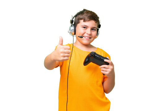Little caucasian kid playing with a video game controller over isolated chroma key background with thumbs up because something good has happened