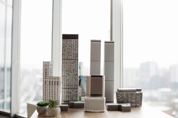 Table with white architectural scale cardboard model of building complex in empty modern architect office. Urban architecture development project for real estate property.