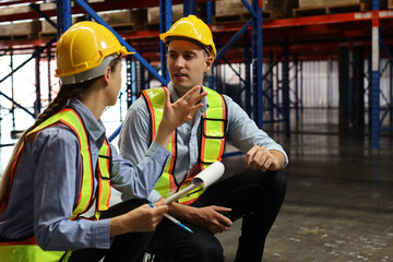 Group of warehouse workers with hardhats and reflective jackets using tablet, walkie talkie radio and cardboard while controlling stock and inventory in retail warehouse logistics, distribution center