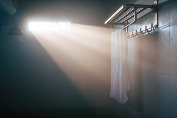 A white towel hangs from a silver fixture in a misty bathroom. The morning light breaks through the...