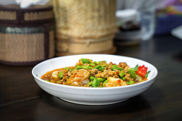 Thai Stir-Fried Stink Beans with Shrimps and spicy shrimp paste sauce in white dish bowl on dark wood table.