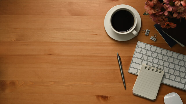 Top view of blank notebook, cup of coffee, pencil holder and keyboard on wooden desk. Copy space for your text