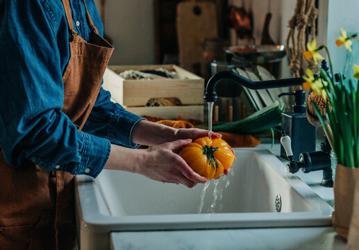 Woman washing tomato under faucet in kitchen