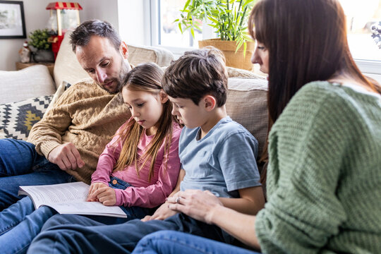 Girl reading book with family in living room at home