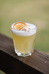 Fresh yeallow gin coctail with tonic and juice. Decorated by a slice of dried orande and cinnamon powder. Wooden table
