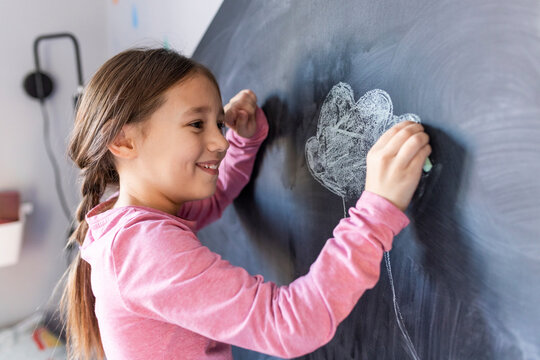 Happy girl drawing with chalk on board at home