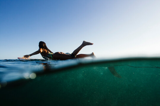 A surfer girl paddles on her longboard over a wave during a before sunset session