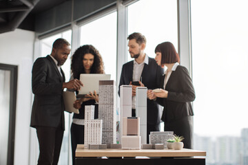 Focus on 3d city model business team of multiethnic corporate workers discussing financial report on digital laptop pc working on building complex prototype project of residential or business district