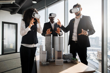 Multiethnic creative business team using virtual reality headsets at the meeting in modern office. Group of developers using virtual reality simulators, standing around table with 3d city model