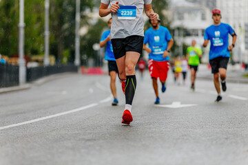 legs man runner in black compression socks run under rain drops on road in city