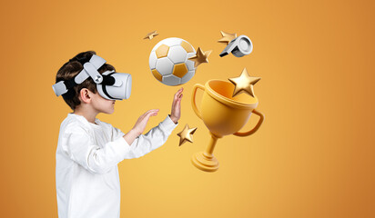 Child boy in vr glasses, hands touching football and champion cup