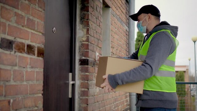Young mailman courier with protective mask is delivering parcel directly to woman buyer customer home with safety. Courier on way to deliver postal parcel to client. Self isolation during quarantine