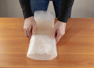 Close-up of a man's hands covering a plastic box with an air bubble wrap at a table in a warehouse