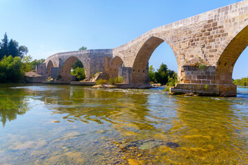 Seljuk Bridge in Aspendos. The Eurymedon Bridge. Crooked bridge, reflected in calm water. An ancient building across the Kopruchay river. Antalya region, Turkey.