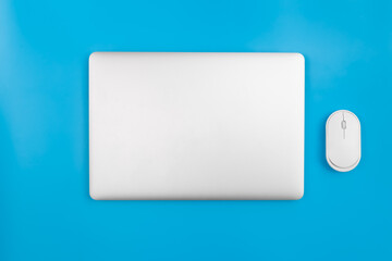 Closed laptop and computer mouse on a blue background, top view.