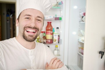 Happy chef standing in front of an open fridge, selecting ingredients for a recipe. 