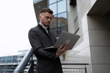 Fototapeta premium young businessman in a coat working on a laptop near the office center