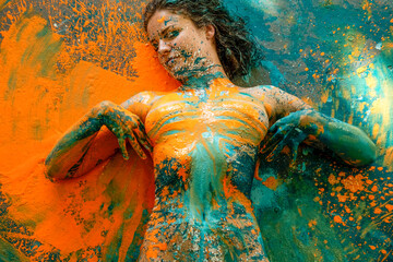 sexy young nude woman in turquoise green and orange color painted decorative, whose fingers have drawn lines in the paint over her painted breasts, creative expressive abstract body painting