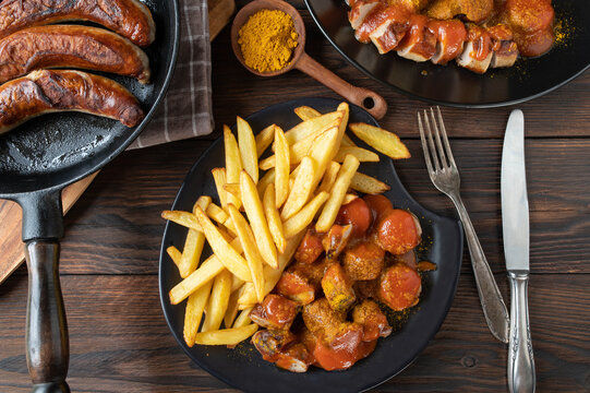 Currywurst or curry sausage with french fries on wooden table. 