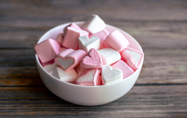 Bowl with marshmallows in the form of hearts, close-up on a wooden background.
