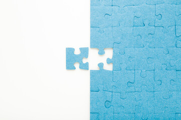 Unfinished blue puzzle with last one piece on white table background. Closeup. Top down view.