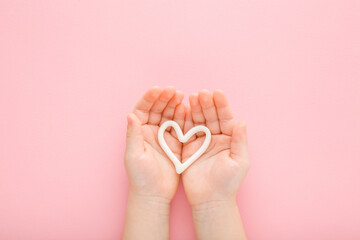 White heart shape on little baby girl opened palms on light pink table background. Pastel color....