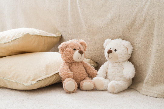 Two smiling white and brown teddy bears sitting on carpet at sofa and pillows at nursery room. Togetherness and friendship concept. Kids best friends. Closeup.