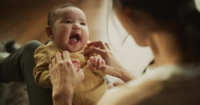 Portrait of a Cute Asian Baby Laughing, Resting on Her Mother's Lap and Enjoying a Bonding Time Together, Looking at her with Love. Playful Mom Tickeling her Toddler and Playing with Her
