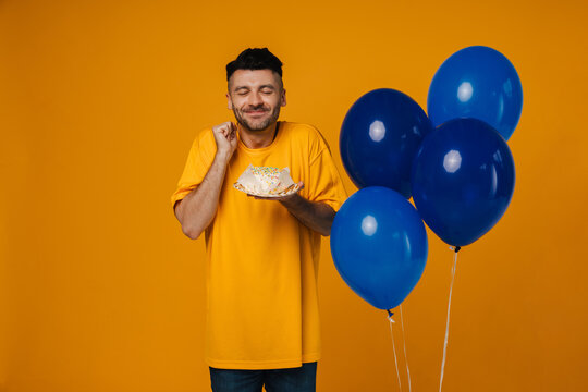 Pleased Man Celebrating Birthday With Air Balloons And Cake Isolated Over Violet Background