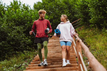 Young man and woman smiling and walking with fitness mats in forest