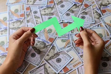 Hand holds green arrow up on dollar bills. Financial growth, interest rate increase, inflation concept.