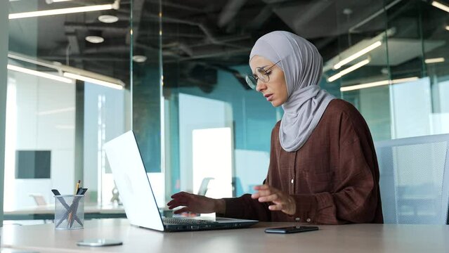 Nervous young muslim businesswoman in hijab feels annoyed has problem with laptop computer in modern office Stressed worker angry because system error data loss backup battery issues bag virus indoors