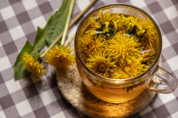 Dandelion flower healthy tea in glass cup on table. Herbal medicine Delicious tisane tea from with fresh yellow blossom dandelion flowers inside tea cup. Green clearing infusion Wildflowers Eco 