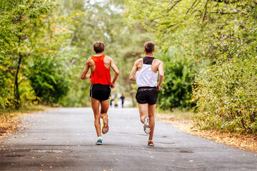 two young athletes runners run race in autumn park