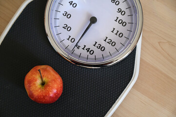 Red apple on an analogue personal scale on a wooden floor, concept for healthy eating, lose weight...