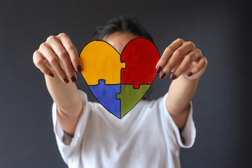 Close-up colorful puzzle heart shape covering face of young girl isolated on gray background....