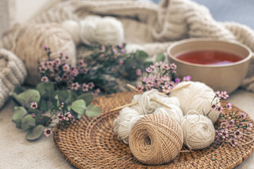 Cozy composition with knitting threads, a cup of tea and flowers.