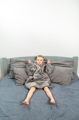 Fototapeta premium A six-year-old boy of European appearance is dressed in gray pajamas, lying and having fun on a gray bed.