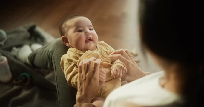 Portrait of a Cute Asian Baby Laughing, Resting on His Mother's Lap and Enjoying a Bonding Time Together, Looking at her with Love. Playful Mom Tickeling her Toddler and Playing with Him