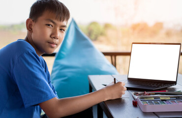 Asian boy wears blue t-shirt and headphone, sitting on pad in front of table and relaxing with drawing and coloring photos which he sketches by himself, recreational activity and free hobby concept.