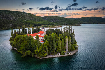 Visovac, Croatia - Aerial view of Visovac Christian monastery island in Krka National Park on a summer morning with green foliage, golden and blue sky at background at sunrise
