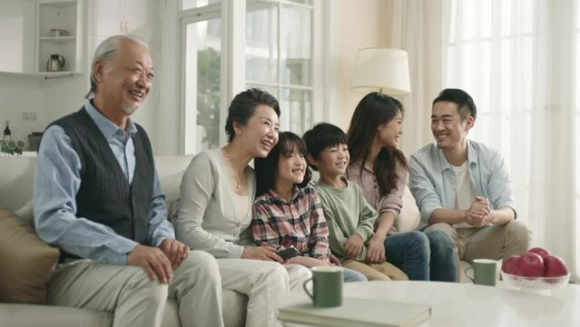 three generation asian family sitting on couch watching tv together at home
