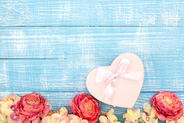 Spring background with flowers and a heart shaped gift box on a blue background.