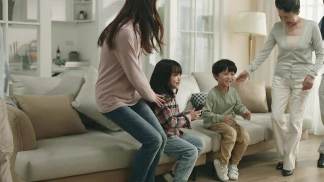 three generation asian family sitting on couch watching tv together at home