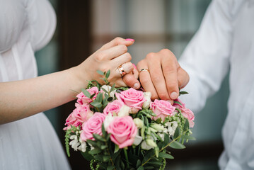 Obraz na płótnie Canvas Wedding rings on the hands of newlyweds. Cropped image of bride and groom crossing little fingers on bouquet of flowers background. Concept of promise. Linking little fingers to confirm promise. Vow.