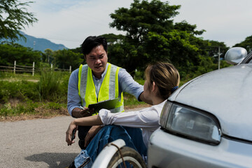 Insurance man talking with driver woman sitting near car after accident on road
