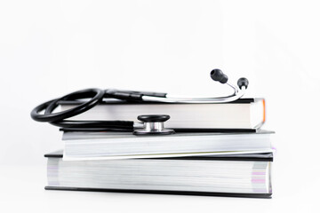 Side view of a stethoscope listening to stacked medicine books on a white background with copy...