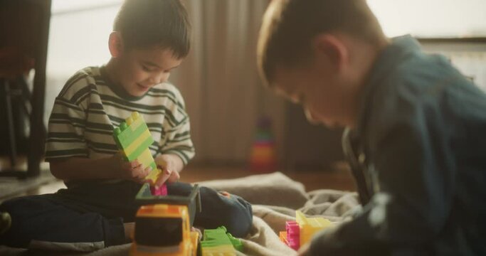 Portrait of Two Male Asian Kids Playing with Colorful Building Blocks in Their Room During the Day. Cute Little Male Child Focused on Making a Toy Castle. Concept of Childhood and Innocence