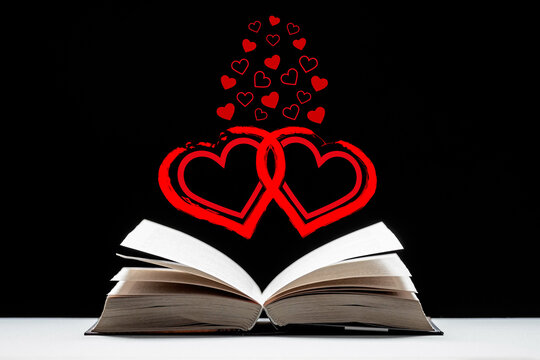 Art book, novel, love story. An open book lies on the table. Red hearts of different sizes on a black background.